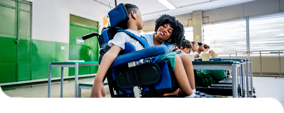 Eine Heilerziehungspflegerin unterst&uuml;tzt ein Kind im Rollstuhl im Unterricht und f&ouml;rdert seine Teilhabe am Schulalltag.