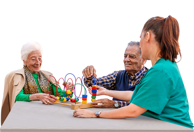 Eine Pflegekraft hilft zwei älteren Menschen, während sie mit bunten Spielzeugen an einem Tisch sitzen